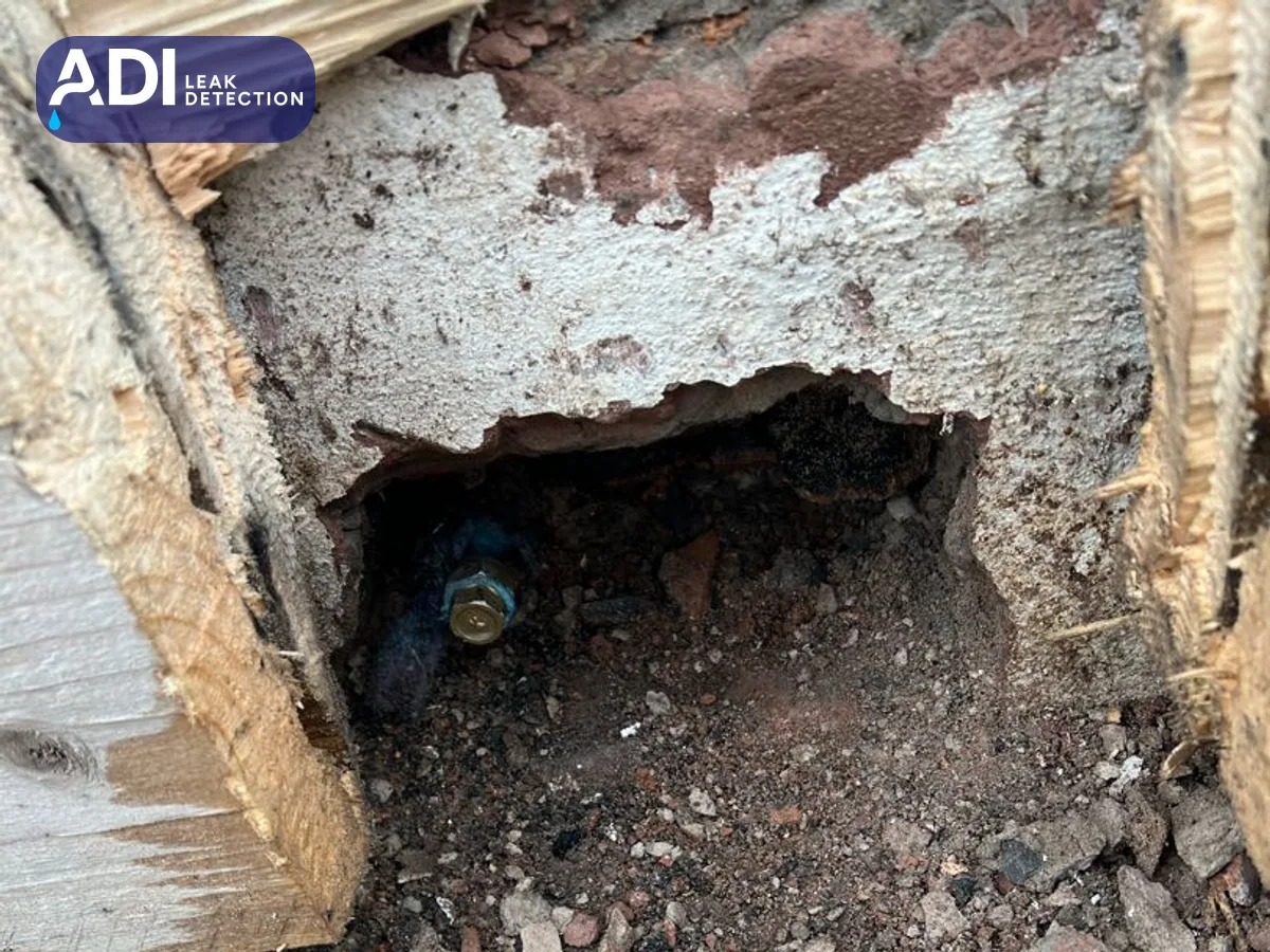 Opening broken into the base of a wall, with a pipe and fitting inside